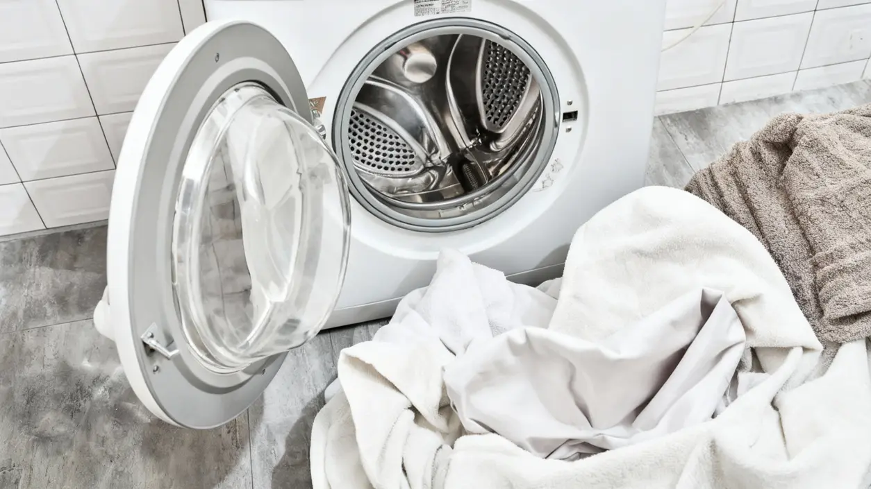 Asciugamani e biancheria davanti a una lavatrice aperta in una lavanderia domestica