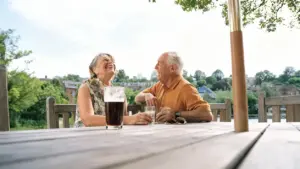 Due persone anziane sorridono sedute a un tavolo all'aperto in un contesto rilassato