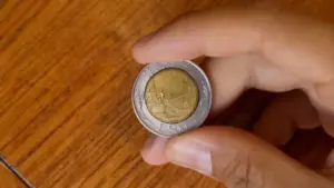 Mano che tiene una moneta da 500 lire italiana su sfondo in legno