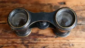 Vecchio binocolo anni '60 in metallo nero appoggiato su un tavolo in legno