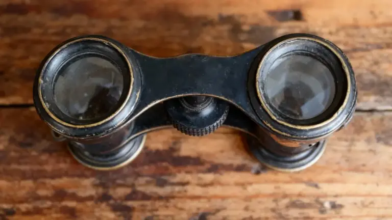 Vecchio binocolo anni '60 in metallo nero appoggiato su un tavolo in legno