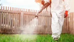 Persona in tuta protettiva che spruzza erbicida su un prato verde