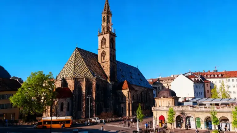 Centro storico con una chiesa medievale e passanti in una piazza soleggiata
